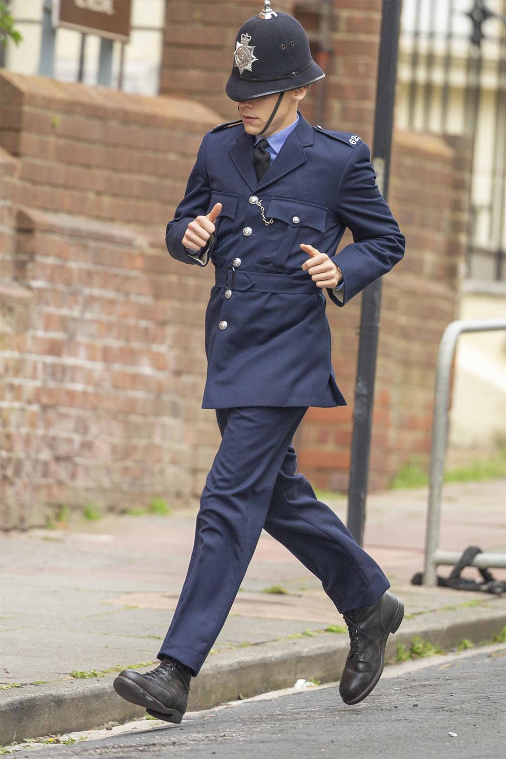 Harry Styles dressed as a  1950's British policeman runs down the street with David Dawson as they film My Policeman in Brighton