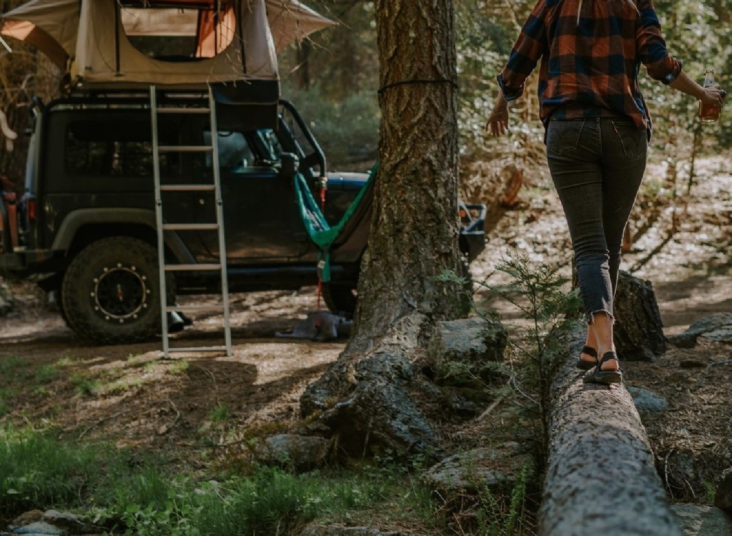 A woman walks across a fallen tree in sandals