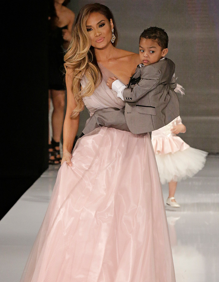 Daphne Joy in a pink dress carrying son Sire