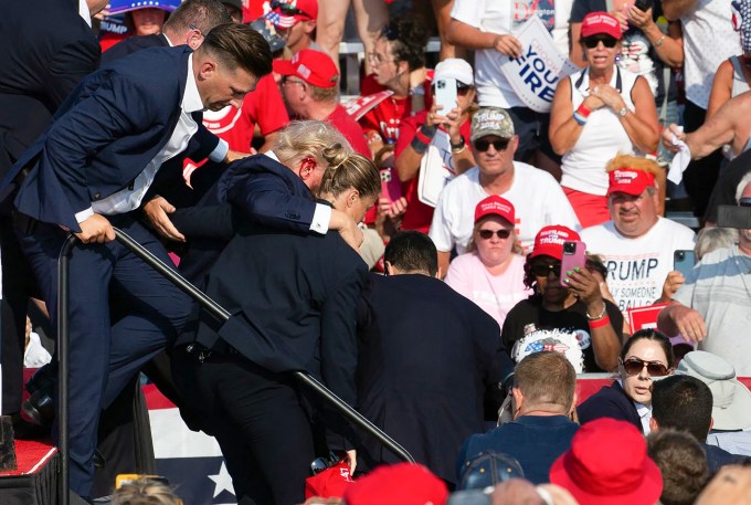 Trump is seen surrounded by secret service agents as he is taken off the stage