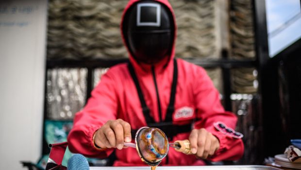 A man dressed as a character from Netflix sensation "Squid Game" makes a crisp sugar candy called a dalgona, the traditional local children's treat featured in the global cultural phenomenon, at his stall in Seoul on November 4, 2021. (Photo by Anthony WALLACE / AFP) (Photo by ANTHONY WALLACE/AFP via Getty Images)