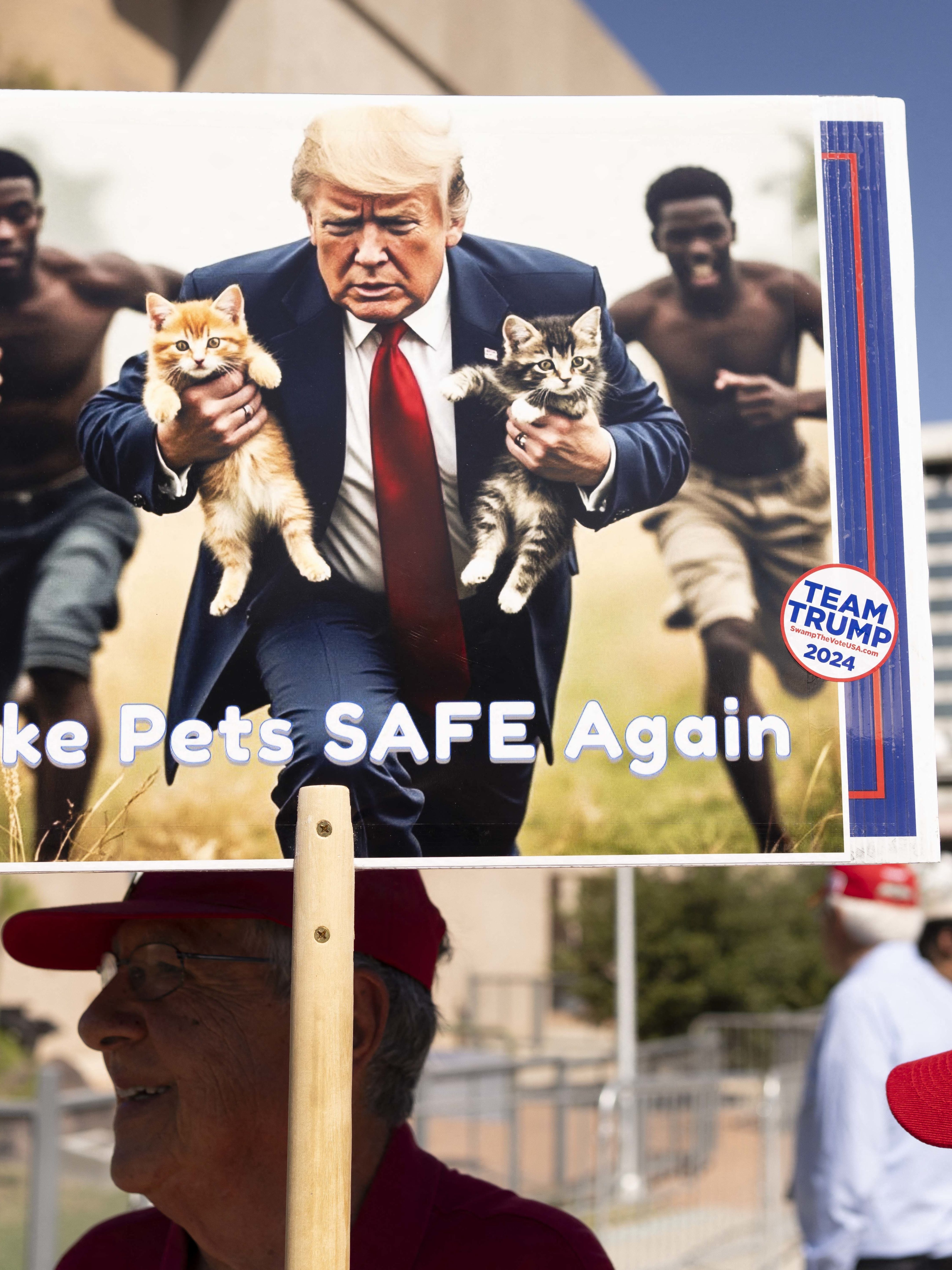 A man carries an AI-generated image of former US President and Republican presidential candidate Donald Trump carrying cats away from Haitian immigrants, a reference to falsehoods spread about Springfield, Ohio, during a campaign rally for Trump at the Tucson Music Hall in Tucson, Arizona, September 12, 2024. (Photo by Rebecca NOBLE / AFP) (Photo by REBECCA NOBLE/AFP via Getty Images)
