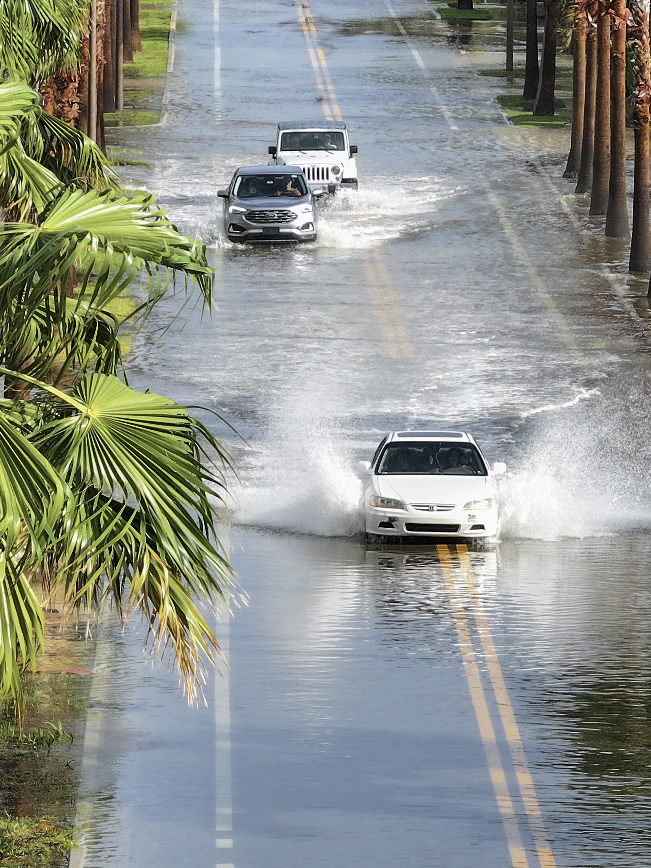 ST. PETE BEACH, FLORIDA - SEPTEMBER 26: In this aerial view, vehicles drive through a flooded street as Hurricane Helene churns offshore on September 26, 2024 in St. Pete Beach, Florida. Later today, Helene is forecast to become a major hurricane, bringing the potential for deadly storm surges, flooding rain, and destructive hurricane-force winds along parts of the Florida West Coast. (Photo by Joe Raedle/Getty Images)