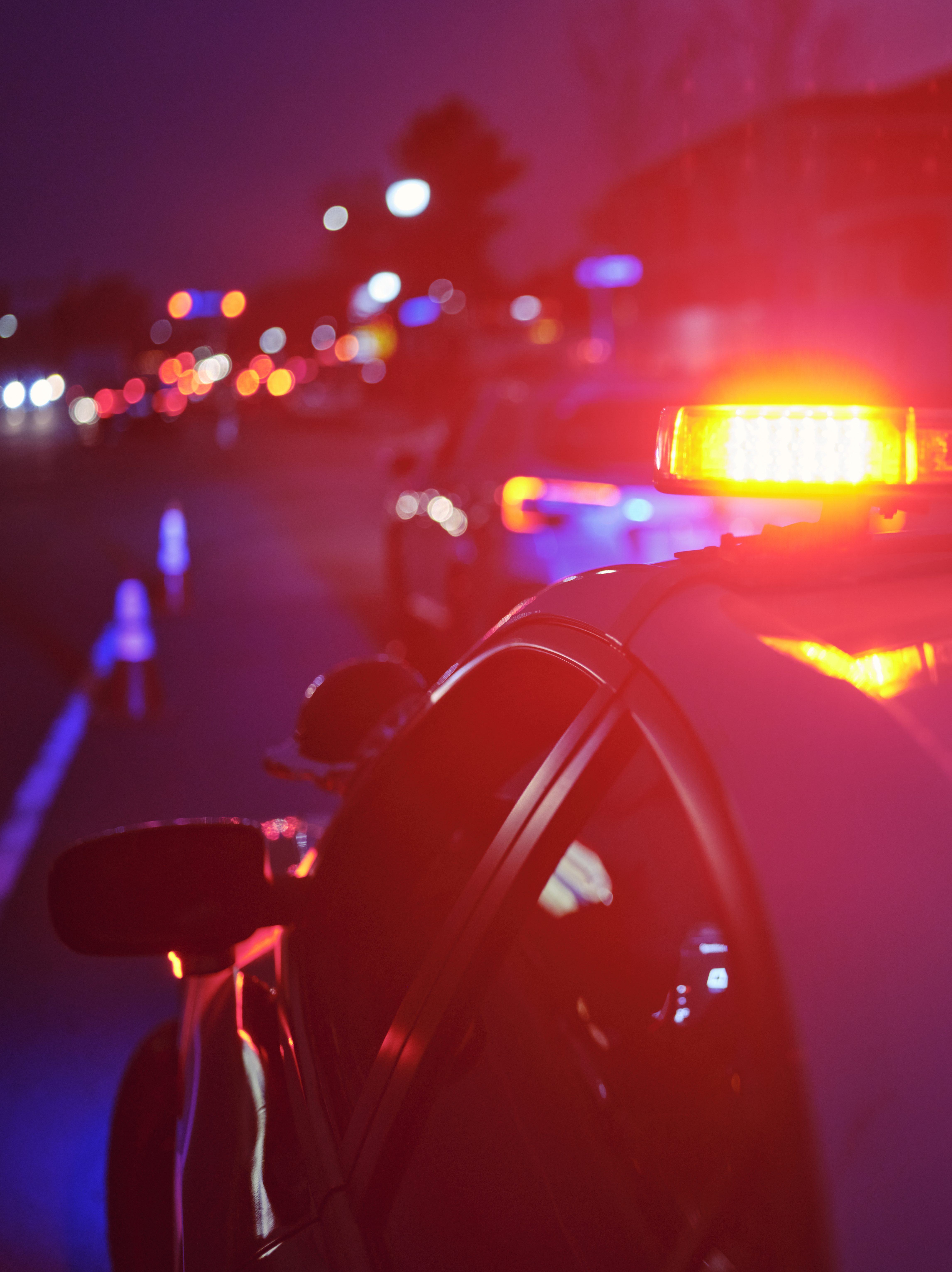 A police car at night alongside a road with emergency lights flashing.
