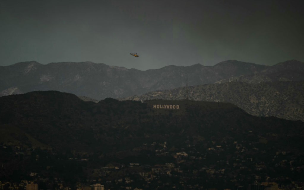 A firefighting helicopter flies above the hollywood sign as the sky is engulfed in dark smoke from the many fires burning around the city, as seen from Kenneth Hahn State Recreation Area in Los Angeles, on January 8, 2025. Rampaging wildfires around Los Angeles have killed at least two people, officials said January 8 as terrifying blazes leveled whole streets, torching cars and houses in minutes.More than 1,000 buildings have burned in multiple wildfires that have erupted around America's second biggest city, forcing tens of thousands of people from their homes. (Photo by Patrick T. Fallon / AFP) (Photo by PATRICK T. FALLON/AFP via Getty Images)